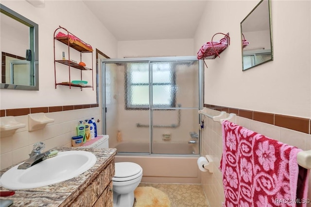 full bathroom with a wainscoted wall, toilet, shower / bath combination with glass door, tile patterned floors, and tile walls