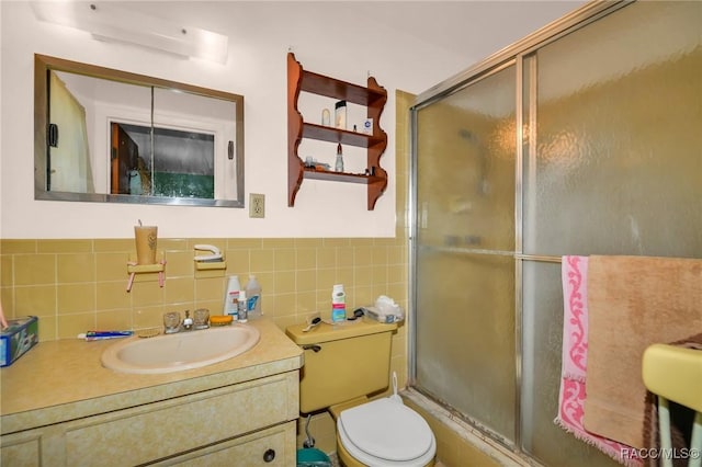 bathroom with toilet, tile walls, a stall shower, and vanity