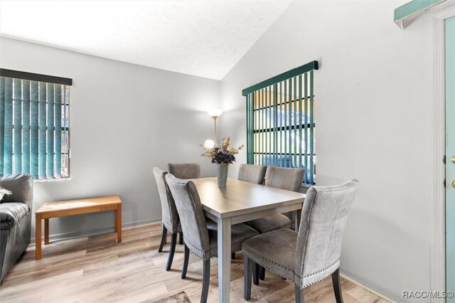 dining room with a textured ceiling, light wood-type flooring, and lofted ceiling