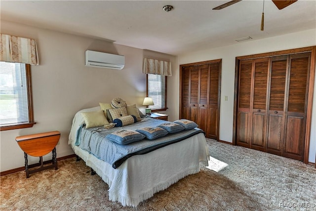 carpeted bedroom with multiple windows, two closets, a wall mounted AC, and ceiling fan