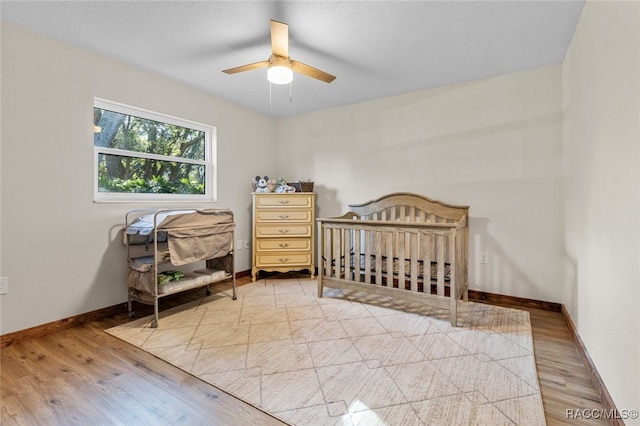 bedroom featuring light wood-type flooring, a nursery area, and ceiling fan