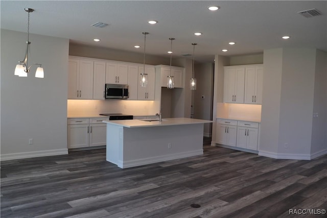 kitchen featuring visible vents, white cabinets, an island with sink, stainless steel microwave, and dark wood-type flooring