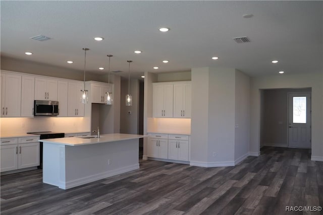 kitchen featuring dark wood-type flooring, a sink, white cabinetry, stainless steel microwave, and an island with sink