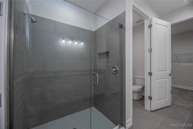 bathroom featuring toilet, tile patterned flooring, and a shower with shower door