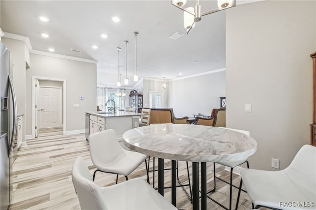 dining space with ornamental molding, sink, an inviting chandelier, and light hardwood / wood-style floors