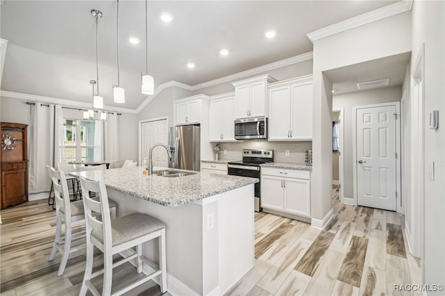 kitchen with appliances with stainless steel finishes, sink, hanging light fixtures, a kitchen island with sink, and light stone countertops