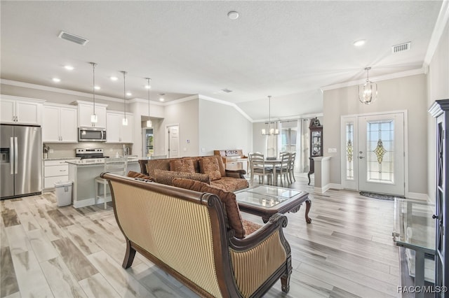 living room with lofted ceiling, a notable chandelier, ornamental molding, and light hardwood / wood-style floors