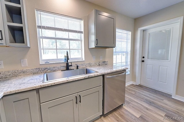 kitchen with light stone countertops, sink, gray cabinets, light wood-type flooring, and stainless steel dishwasher