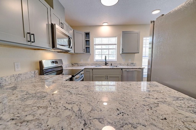 kitchen with stainless steel appliances, gray cabinetry, a textured ceiling, light stone counters, and sink