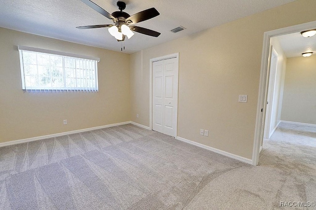 unfurnished bedroom with a textured ceiling, ceiling fan, a closet, and light colored carpet