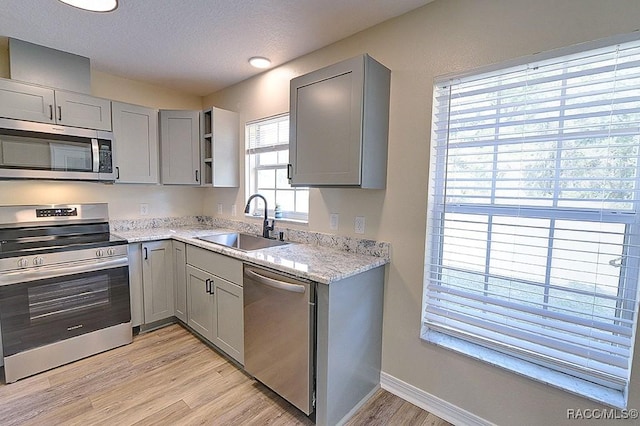 kitchen with gray cabinets, appliances with stainless steel finishes, light hardwood / wood-style floors, and sink