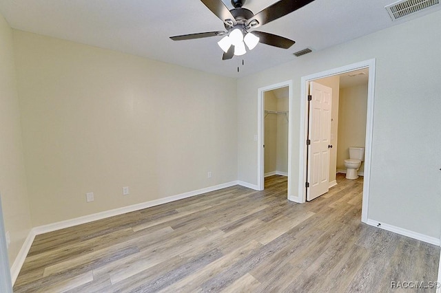 unfurnished bedroom with a spacious closet, connected bathroom, a closet, light wood-type flooring, and ceiling fan