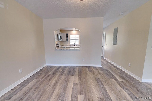 empty room featuring hardwood / wood-style flooring, sink, a textured ceiling, and electric panel