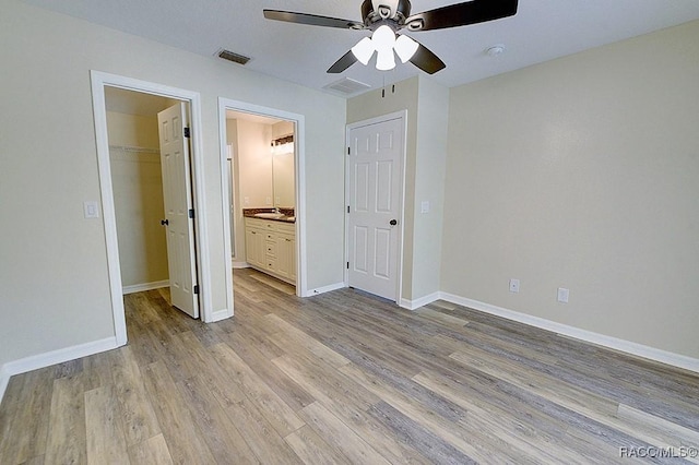 unfurnished bedroom featuring ceiling fan, light hardwood / wood-style floors, connected bathroom, a walk in closet, and a closet