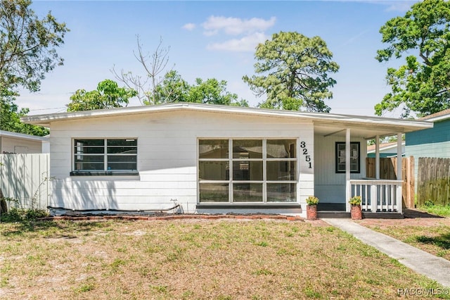 view of front facade with covered porch, a front lawn, and fence