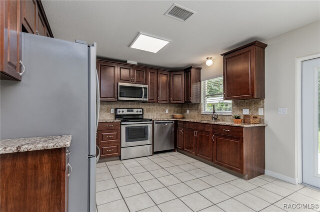 kitchen with backsplash, light stone counters, dark brown cabinets, stainless steel appliances, and light tile patterned floors