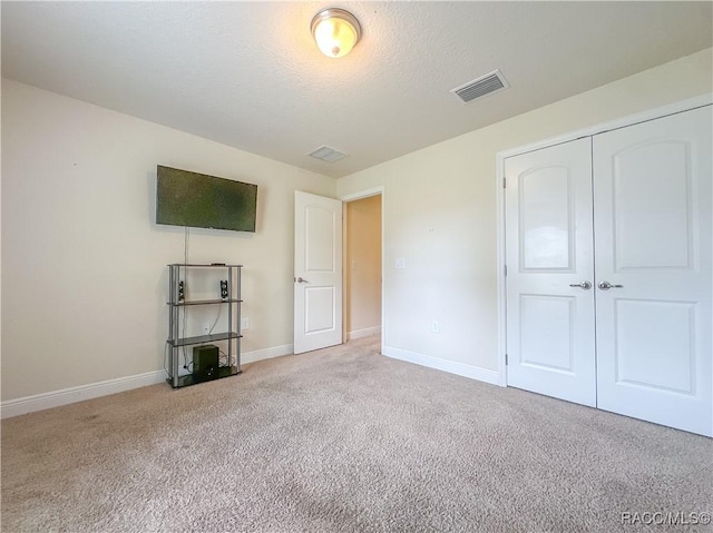 unfurnished bedroom with light carpet, baseboards, visible vents, a textured ceiling, and a closet