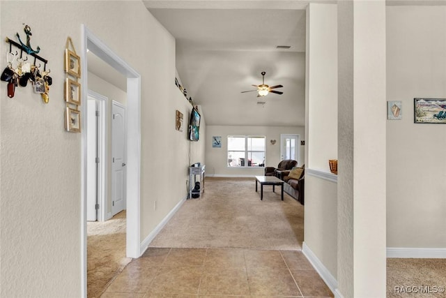 corridor with light carpet, light tile patterned floors, baseboards, and vaulted ceiling