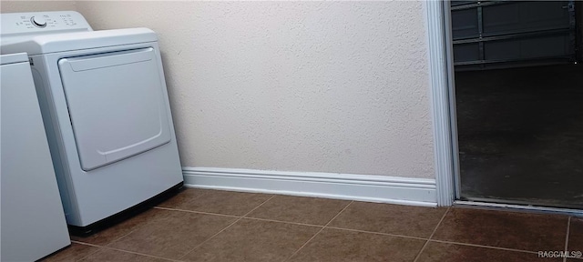 laundry room with dark tile patterned floors, baseboards, washer and clothes dryer, and a textured wall