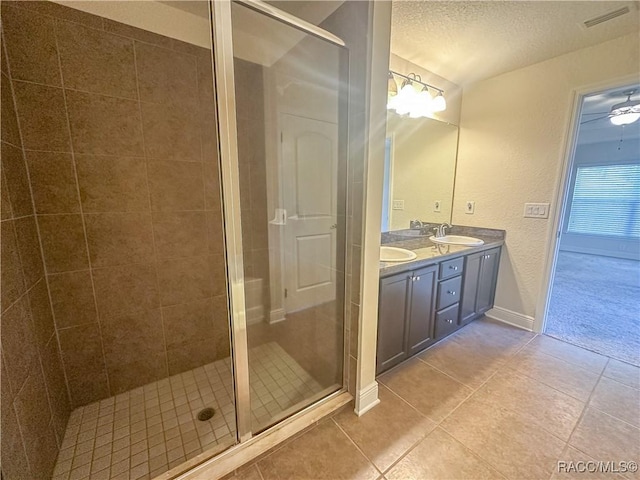 bathroom featuring double vanity, a stall shower, a sink, a textured ceiling, and tile patterned floors