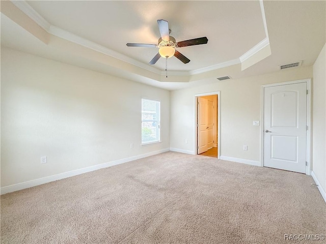 unfurnished bedroom featuring a tray ceiling, light colored carpet, visible vents, ornamental molding, and baseboards