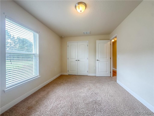 unfurnished bedroom with carpet floors, a closet, visible vents, a textured ceiling, and baseboards