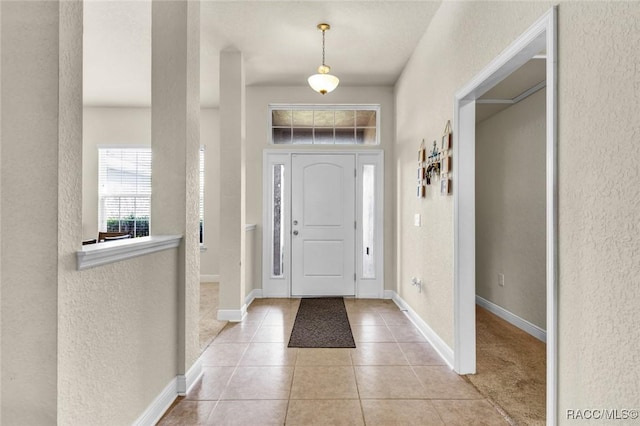 entryway with light tile patterned floors, a textured wall, and baseboards