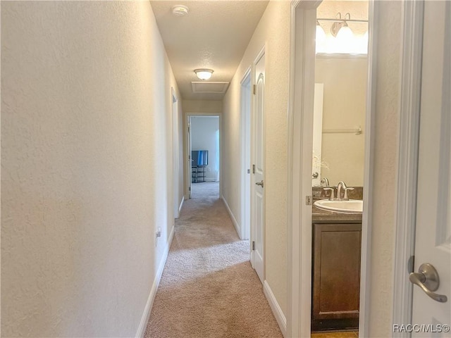 corridor with attic access, baseboards, a textured wall, light colored carpet, and a sink