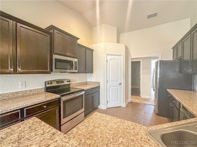 unfurnished living room featuring vaulted ceiling, ceiling fan with notable chandelier, and dark tile patterned flooring