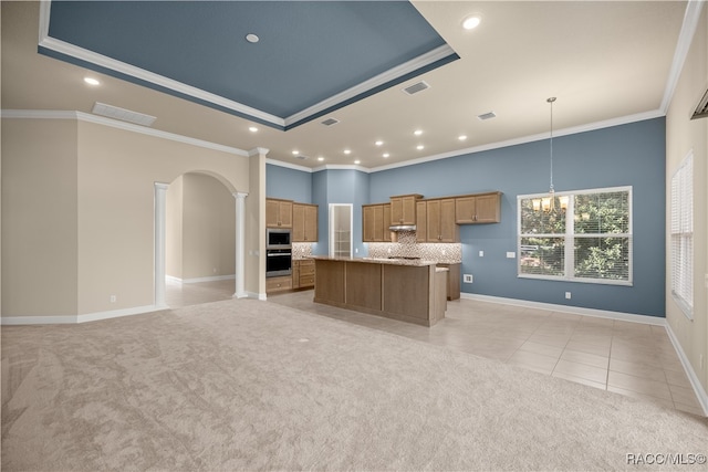 kitchen featuring ornamental molding, light colored carpet, a tray ceiling, a center island, and hanging light fixtures