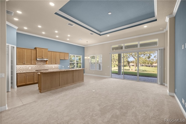 kitchen featuring a center island with sink, a raised ceiling, light colored carpet, and crown molding