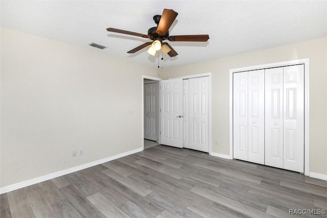 unfurnished bedroom featuring ceiling fan, wood-type flooring, and two closets