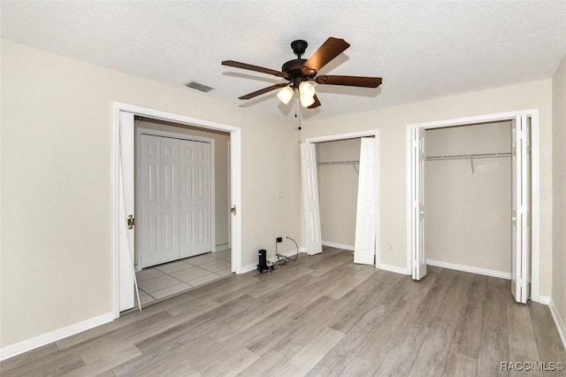 unfurnished bedroom with ceiling fan, two closets, a textured ceiling, and light wood-type flooring