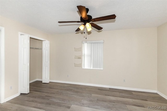 unfurnished bedroom with a textured ceiling, ceiling fan, a closet, and hardwood / wood-style floors