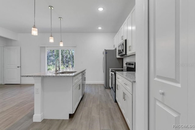 kitchen with stainless steel appliances, sink, pendant lighting, white cabinetry, and an island with sink