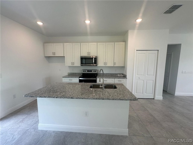 kitchen with stainless steel appliances, sink, dark stone countertops, white cabinetry, and an island with sink