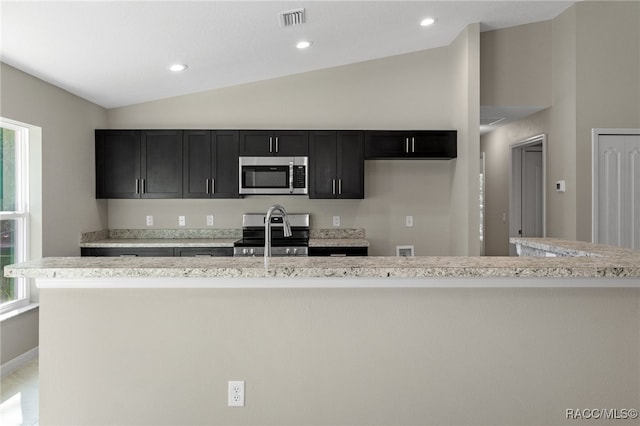 kitchen with light stone counters, a kitchen island with sink, appliances with stainless steel finishes, and vaulted ceiling