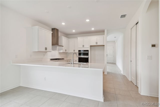 kitchen featuring kitchen peninsula, wall chimney exhaust hood, sink, white cabinetry, and light tile patterned floors