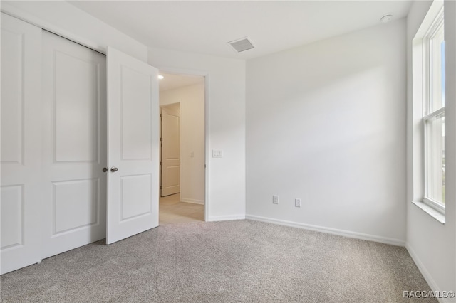 unfurnished bedroom with multiple windows, a closet, and light carpet