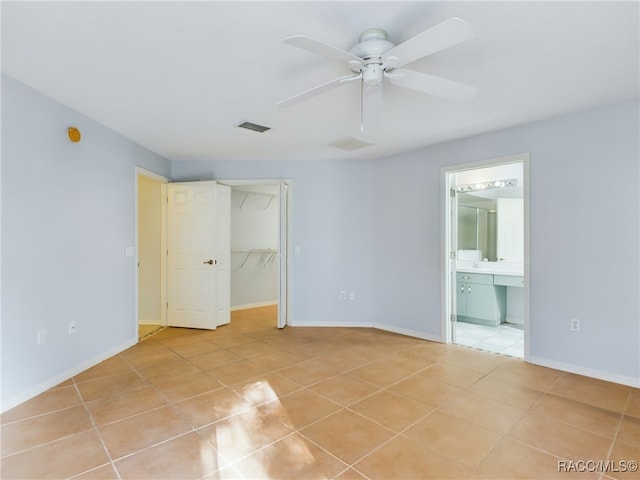 unfurnished bedroom featuring ensuite bathroom, a walk in closet, ceiling fan, light tile patterned flooring, and a closet