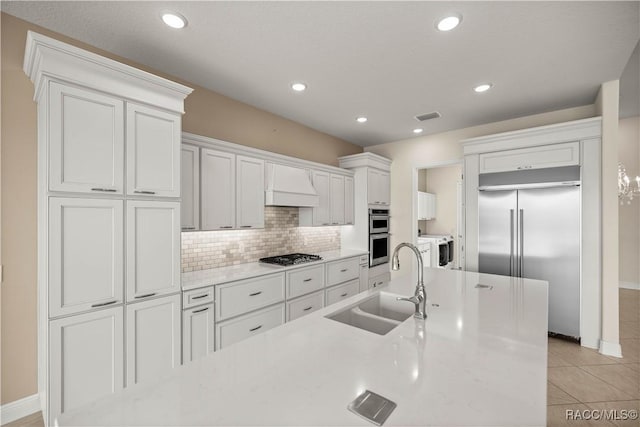 kitchen with sink, custom exhaust hood, white cabinetry, stainless steel appliances, and backsplash