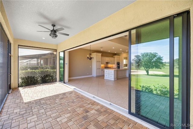 unfurnished sunroom with ceiling fan with notable chandelier