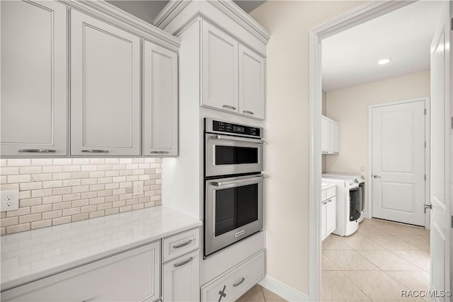 kitchen with light tile patterned floors, washer and clothes dryer, double oven, and white cabinets