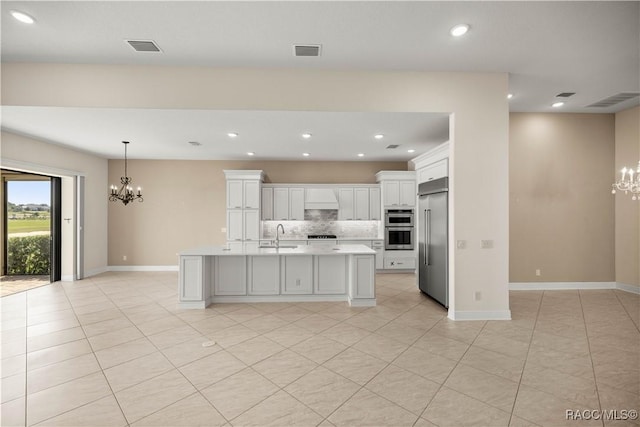 kitchen with appliances with stainless steel finishes, white cabinetry, tasteful backsplash, a center island with sink, and a chandelier