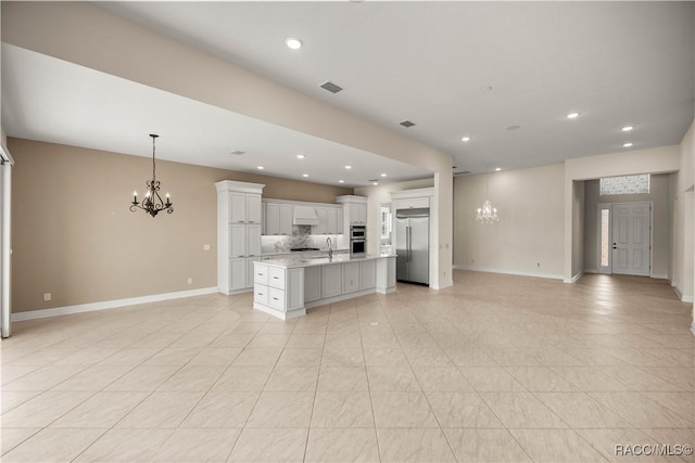 kitchen with an inviting chandelier, white cabinetry, hanging light fixtures, an island with sink, and stainless steel appliances