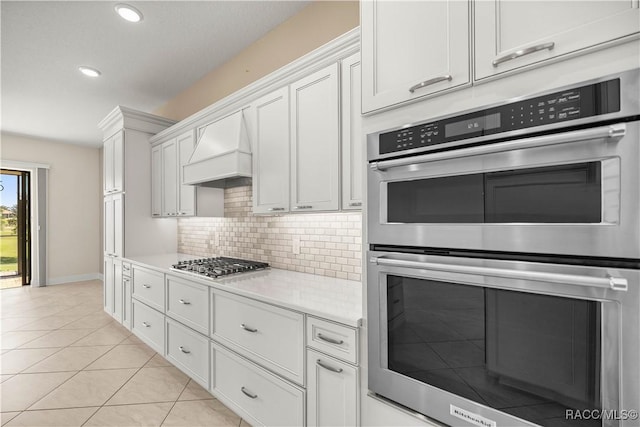 kitchen featuring light tile patterned flooring, appliances with stainless steel finishes, tasteful backsplash, white cabinets, and custom range hood