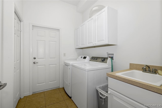 clothes washing area featuring washing machine and dryer, sink, light tile patterned floors, and cabinets