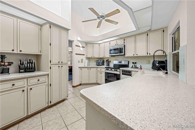 kitchen featuring stainless steel appliances, cream cabinets, sink, and a tray ceiling