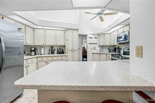 kitchen with lofted ceiling, light tile patterned floors, ceiling fan, appliances with stainless steel finishes, and kitchen peninsula