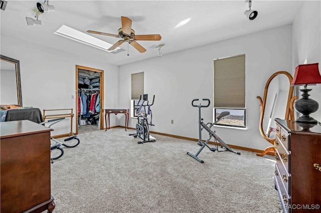 workout area with ceiling fan, light colored carpet, and a skylight